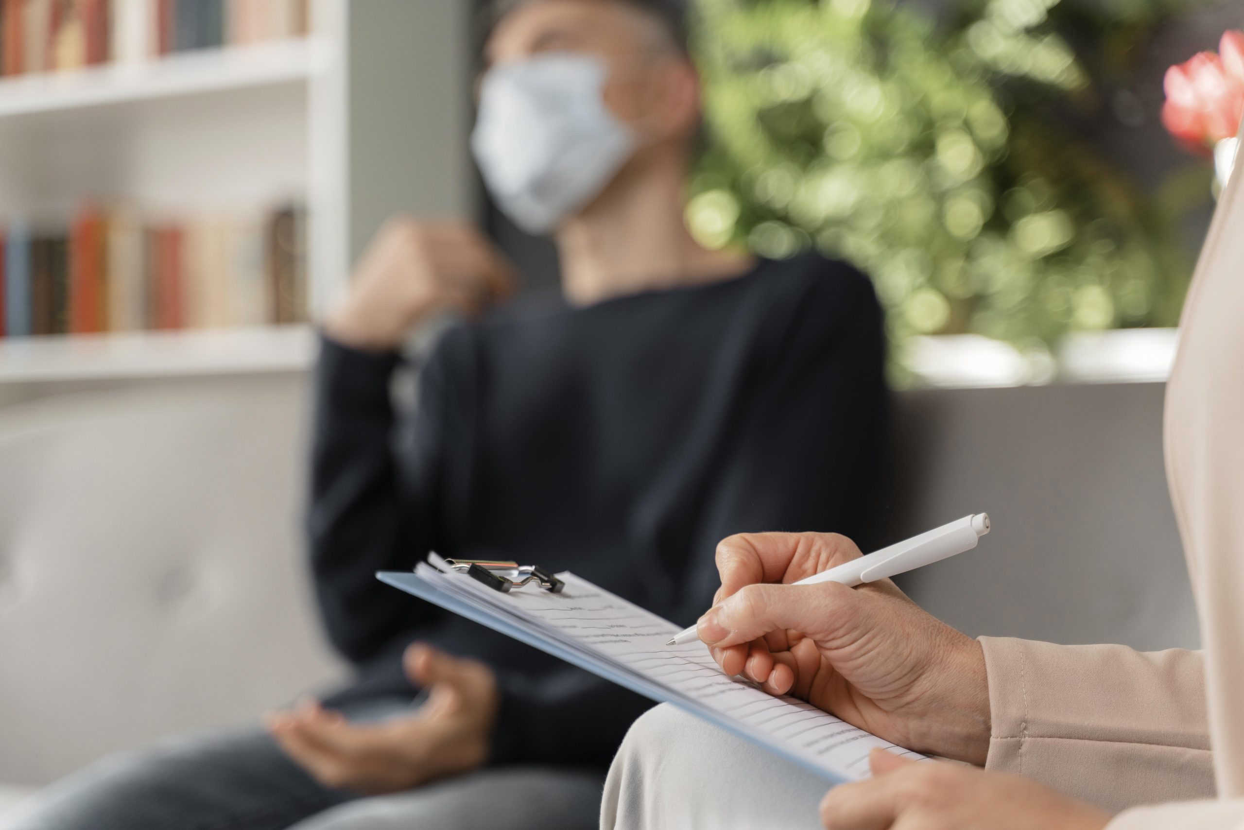 woman-therapist-taking-notes-man-therapy-office-with-mask