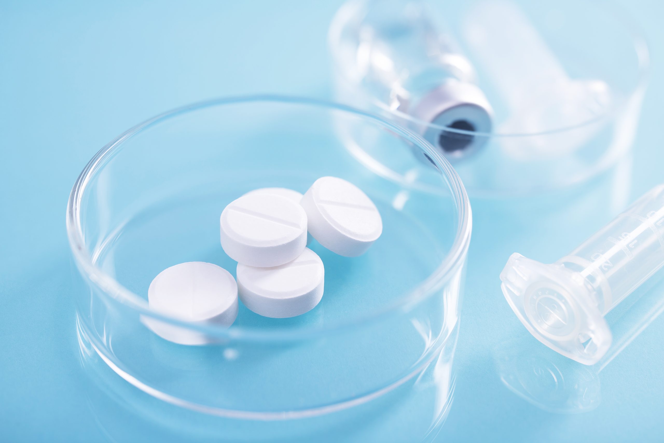 Closeup shot of white pills in a glass dish at a lab